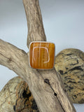 A square agate ring in sterling silver ring featuring a polished waterline carnelian stone, displayed on a piece of driftwood.