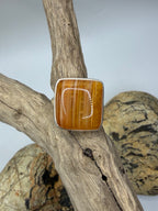 A square agate ring in sterling silver ring featuring a polished waterline carnelian stone, displayed on a piece of driftwood.